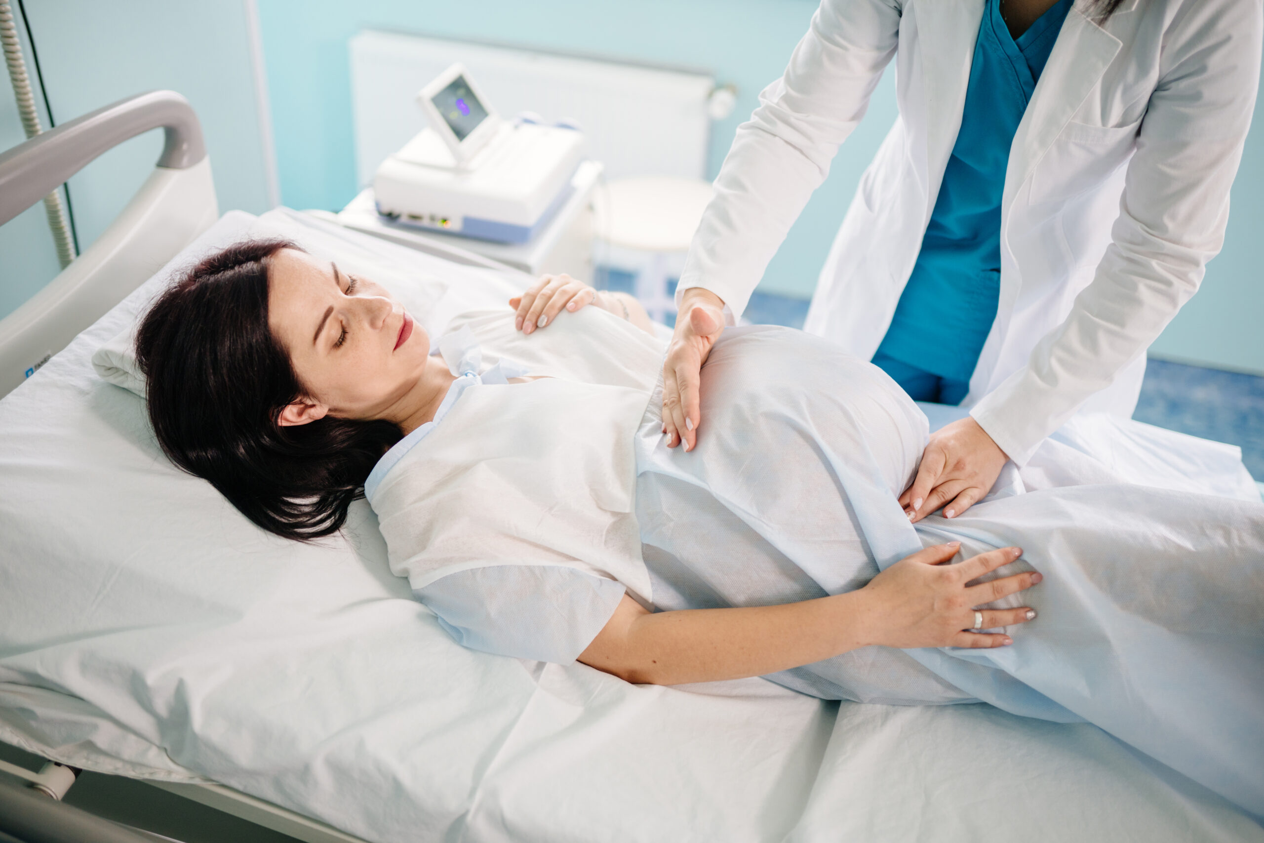 Pregnant woman lying on medical couch while professional gynecologist doing palpation of her tummy. Female doctor examining female patient before childbirth at modern clinic.