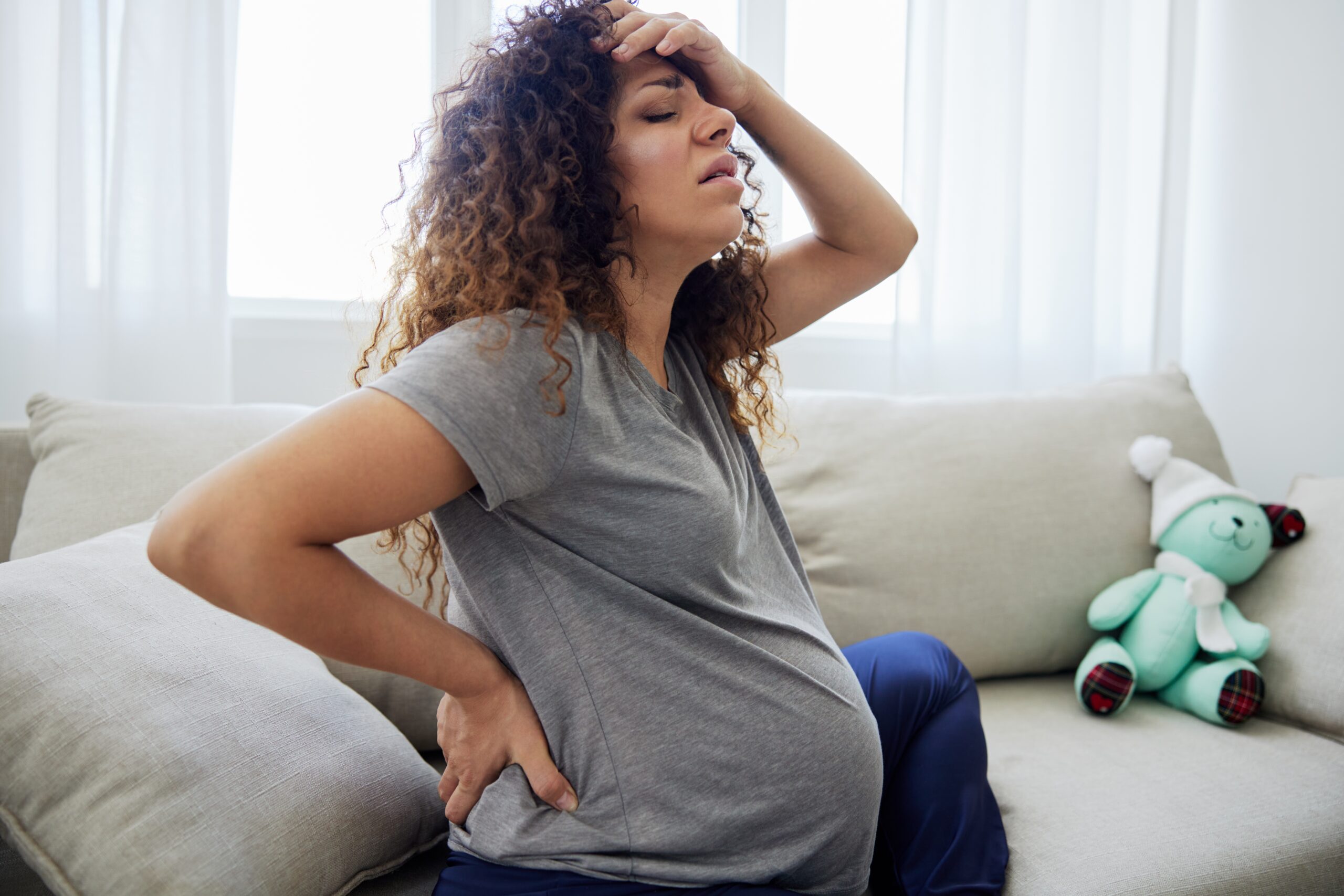 Pregnant woman sitting on the couch lower back pain and headache, strain on the spine during pregnancy. Lifestyle preparation for childbirth, last month of pregnancy. High quality photo